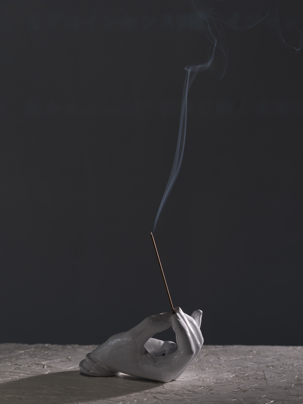 陶器の手が線香を灯す静物写真