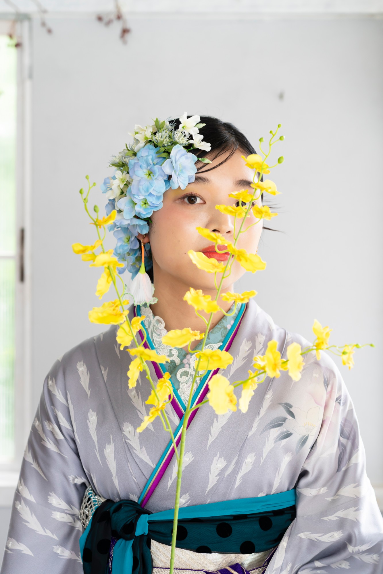 黄色いオンシジウムの花越しに見つめる、青い花の髪飾りの女性