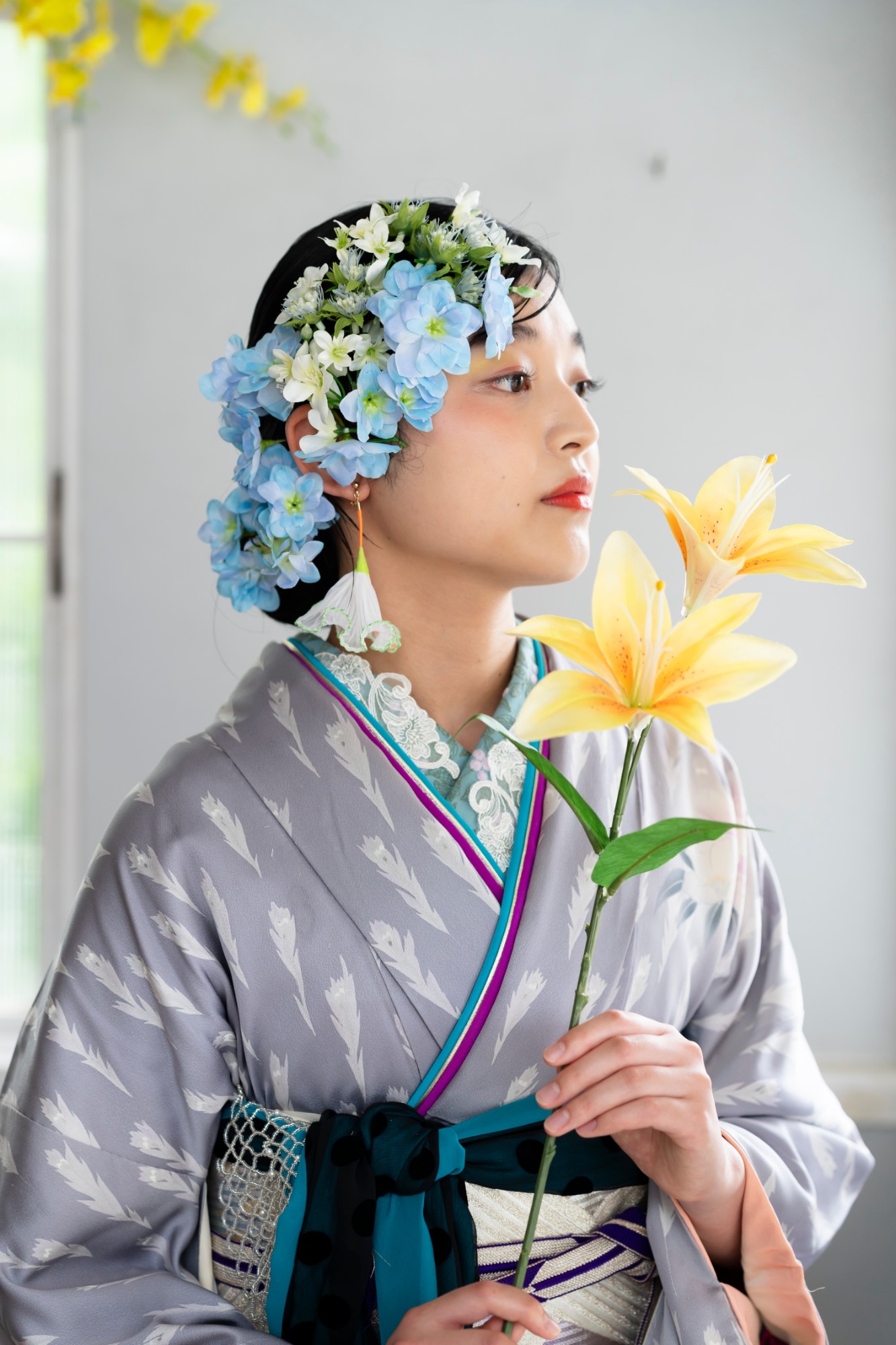 黄色いユリの花を手に、横を向く青い花の髪飾りの女性