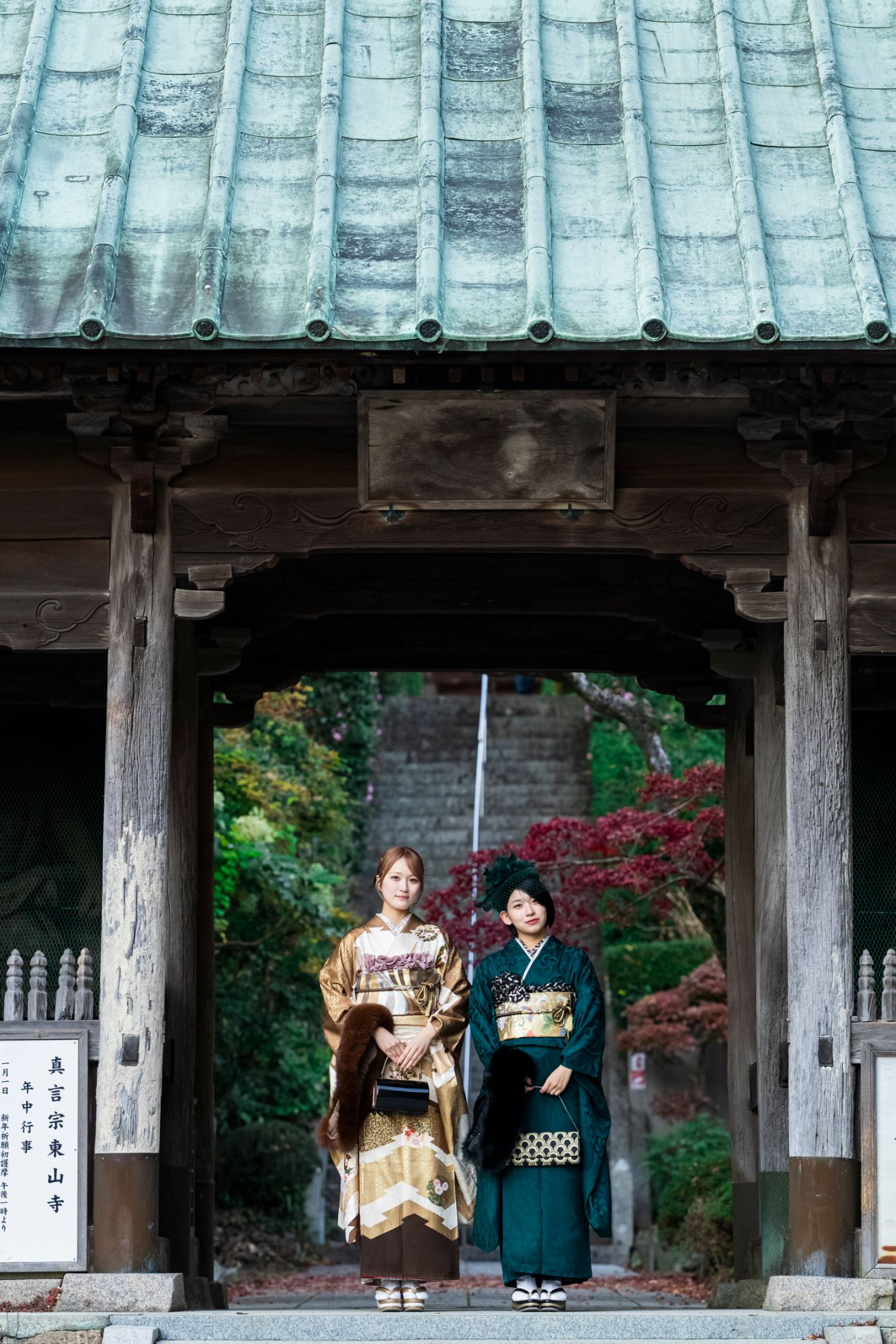 お寺の門の前に立つ、振袖姿の二人