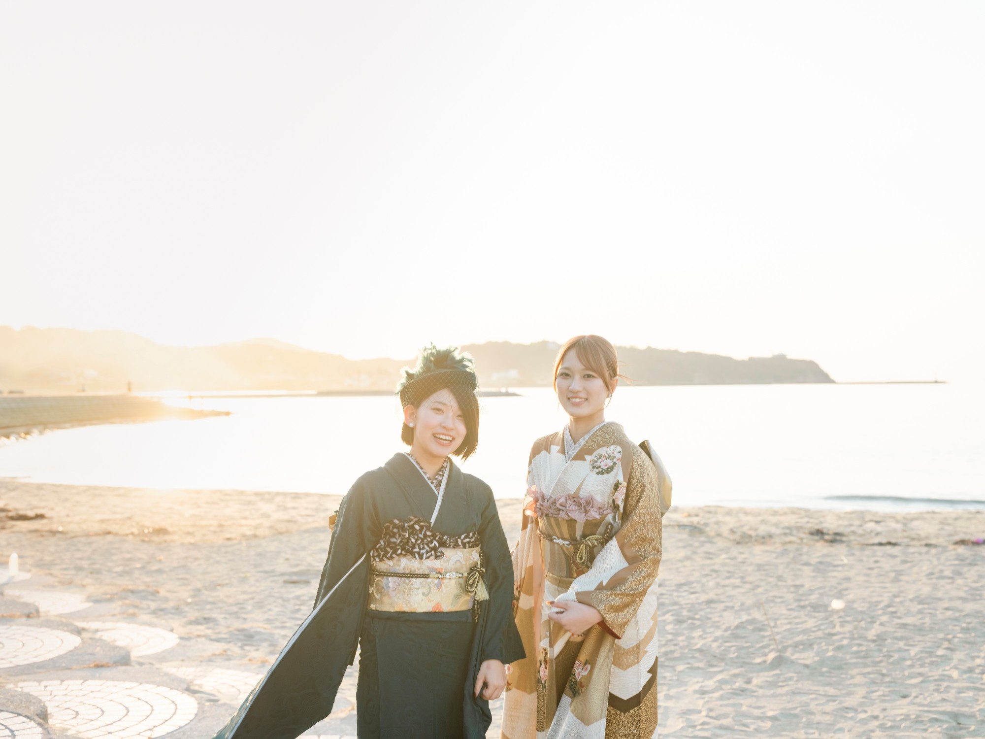 夕方の海辺で、振袖姿で笑顔を見せる二人