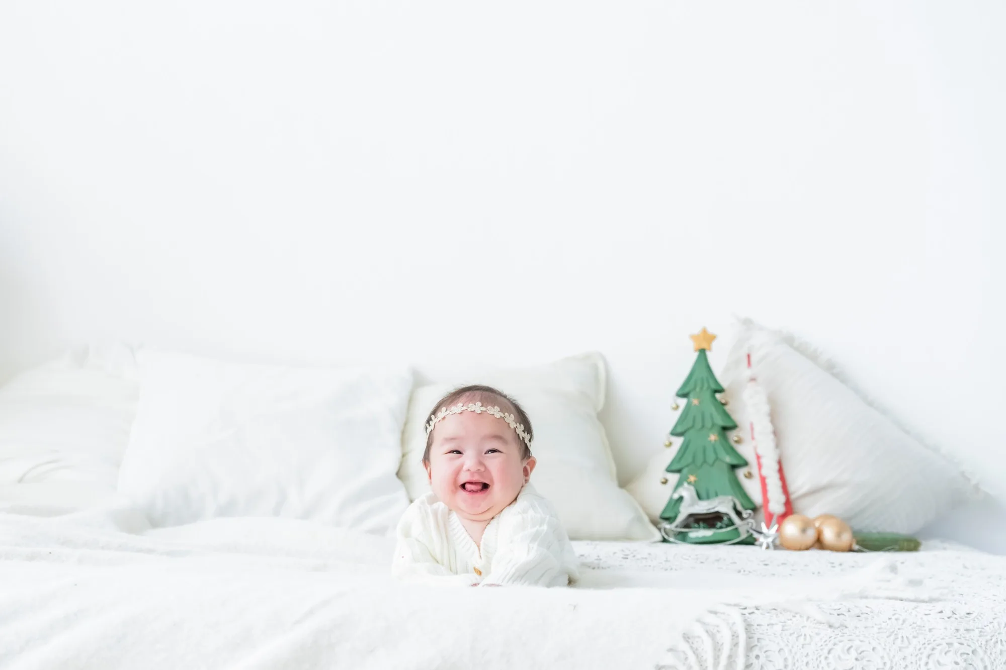 クリスマスツリーの飾りのそばで、ベッドの上で笑う赤ちゃん