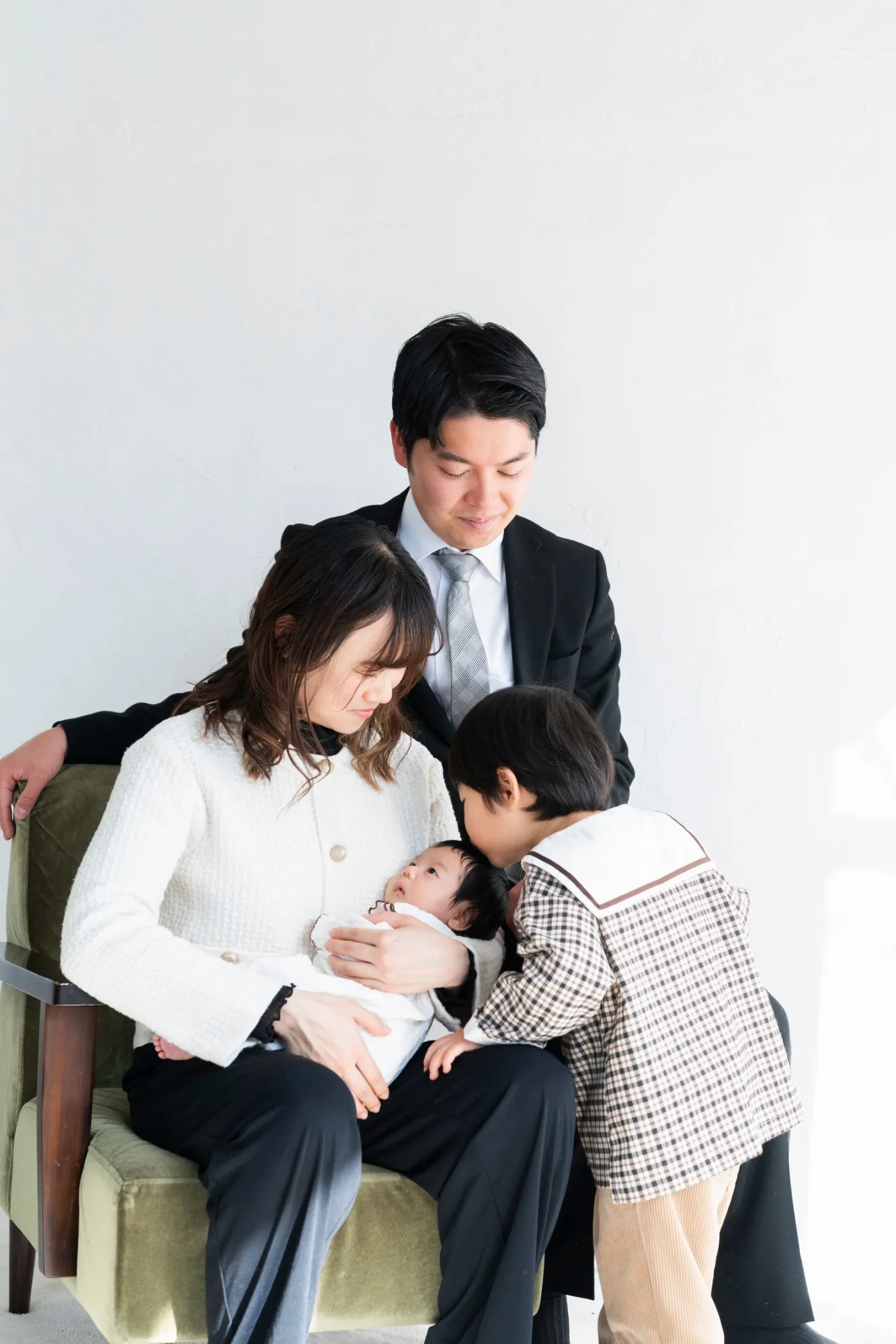 ソファで新生児を見つめる家族と、寄り添うきょうだい