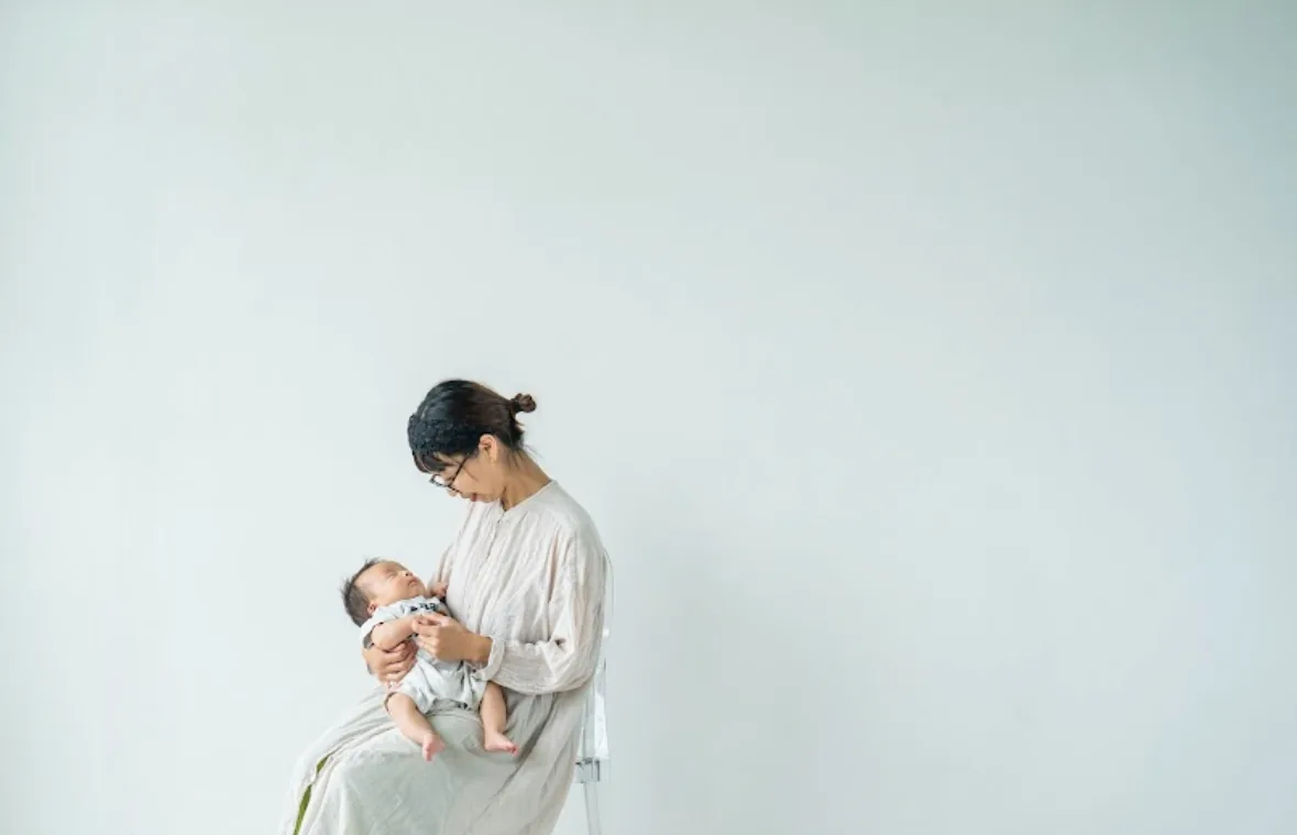 椅子に座り、新生児を見つめる母親
