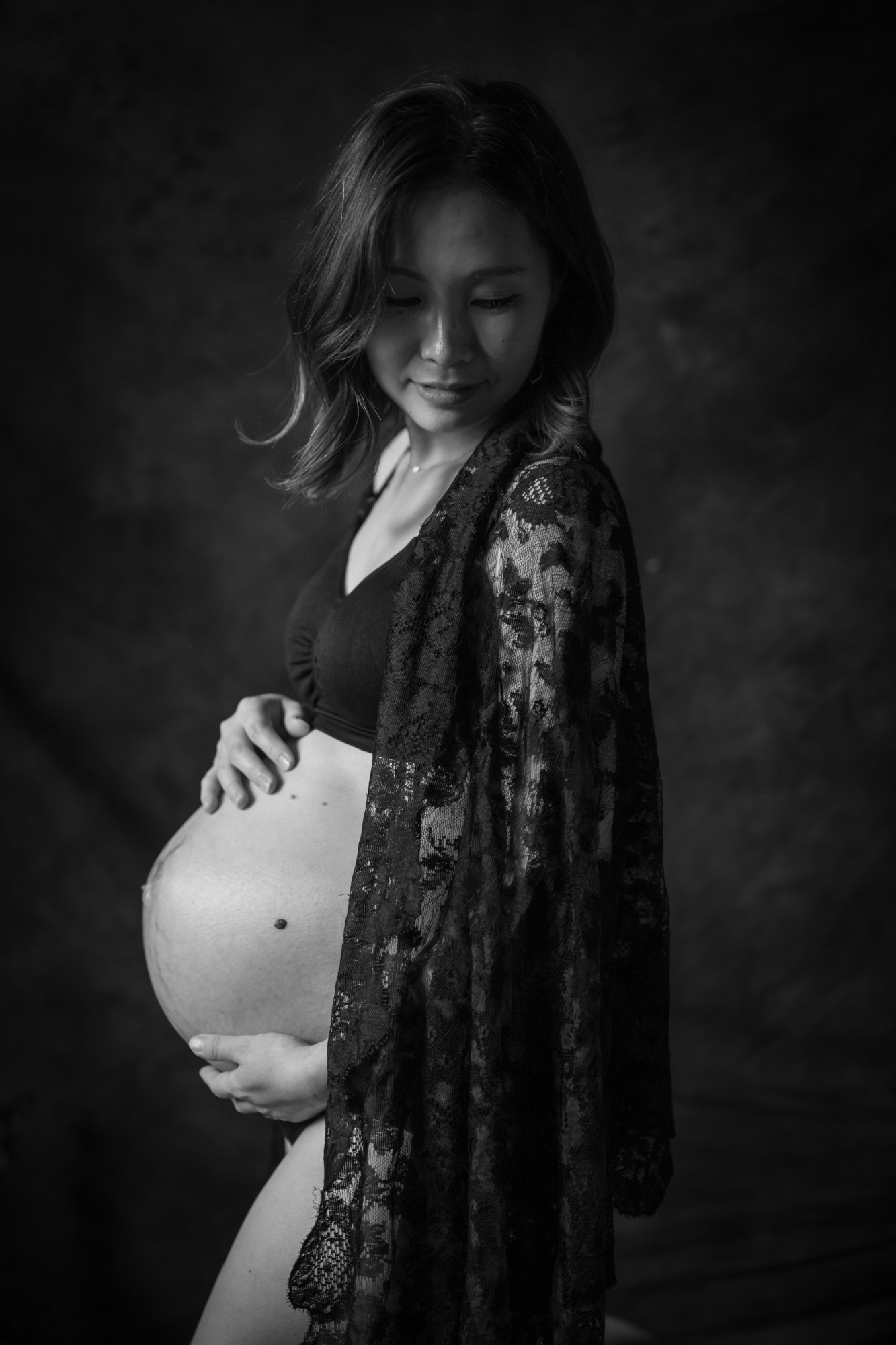 黒いレースをまとい、お腹に手を添える妊娠中の女性のモノクロポートレート