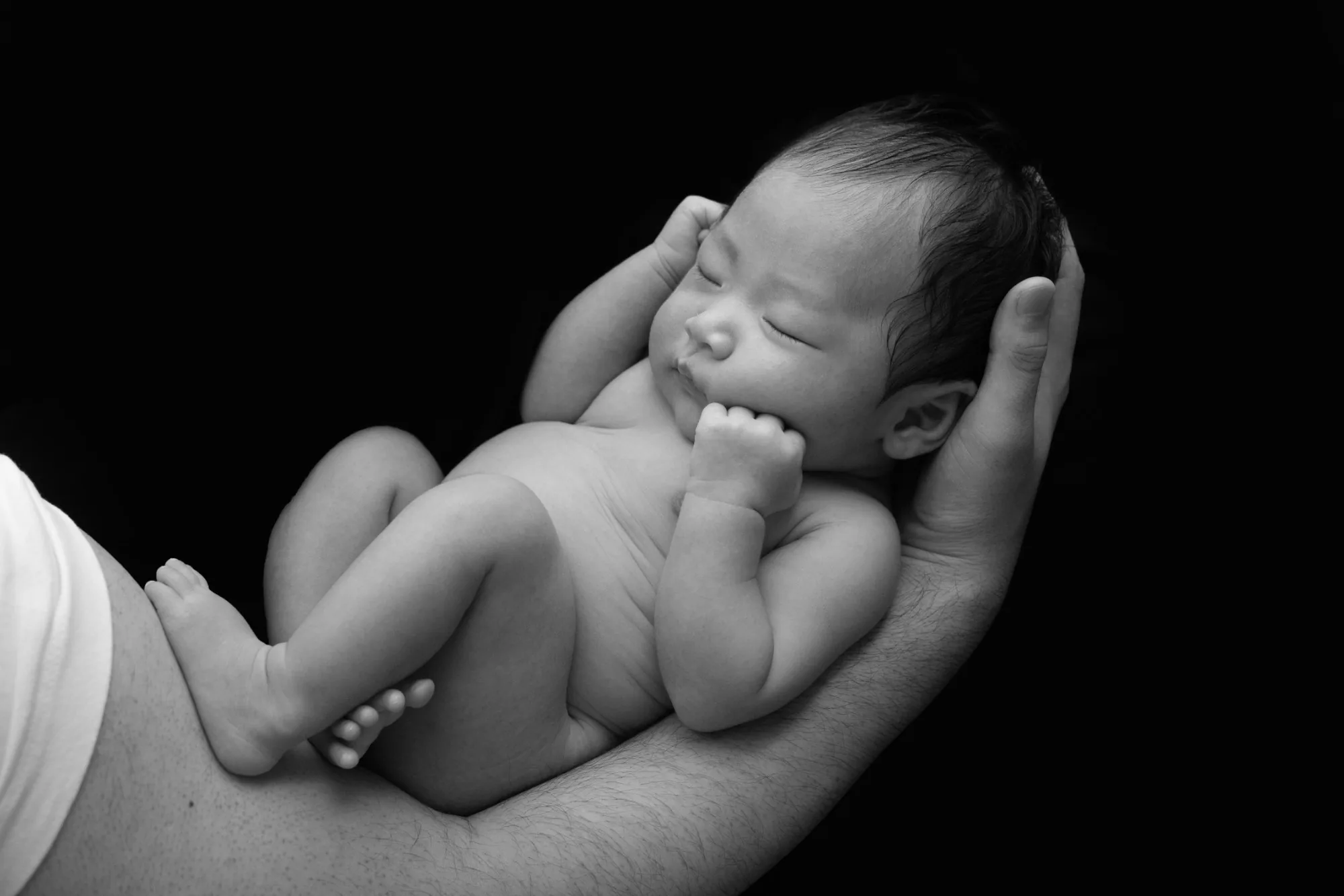 大人の両手にそっと抱かれる新生児(モノクロ)