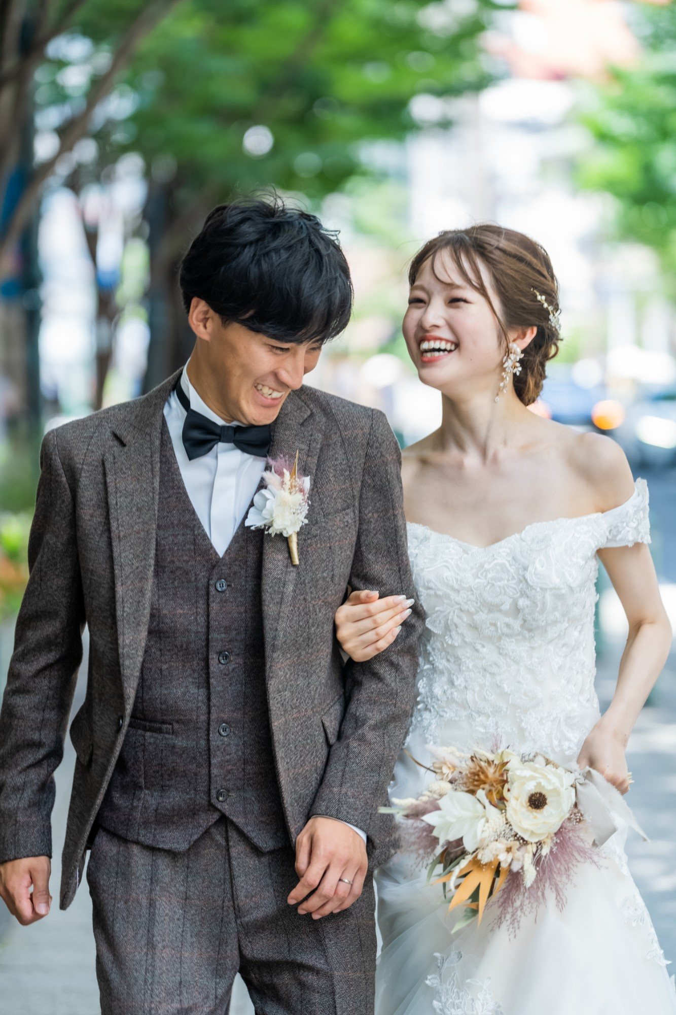 街路樹の下で腕を組み、笑い合う新郎新婦
