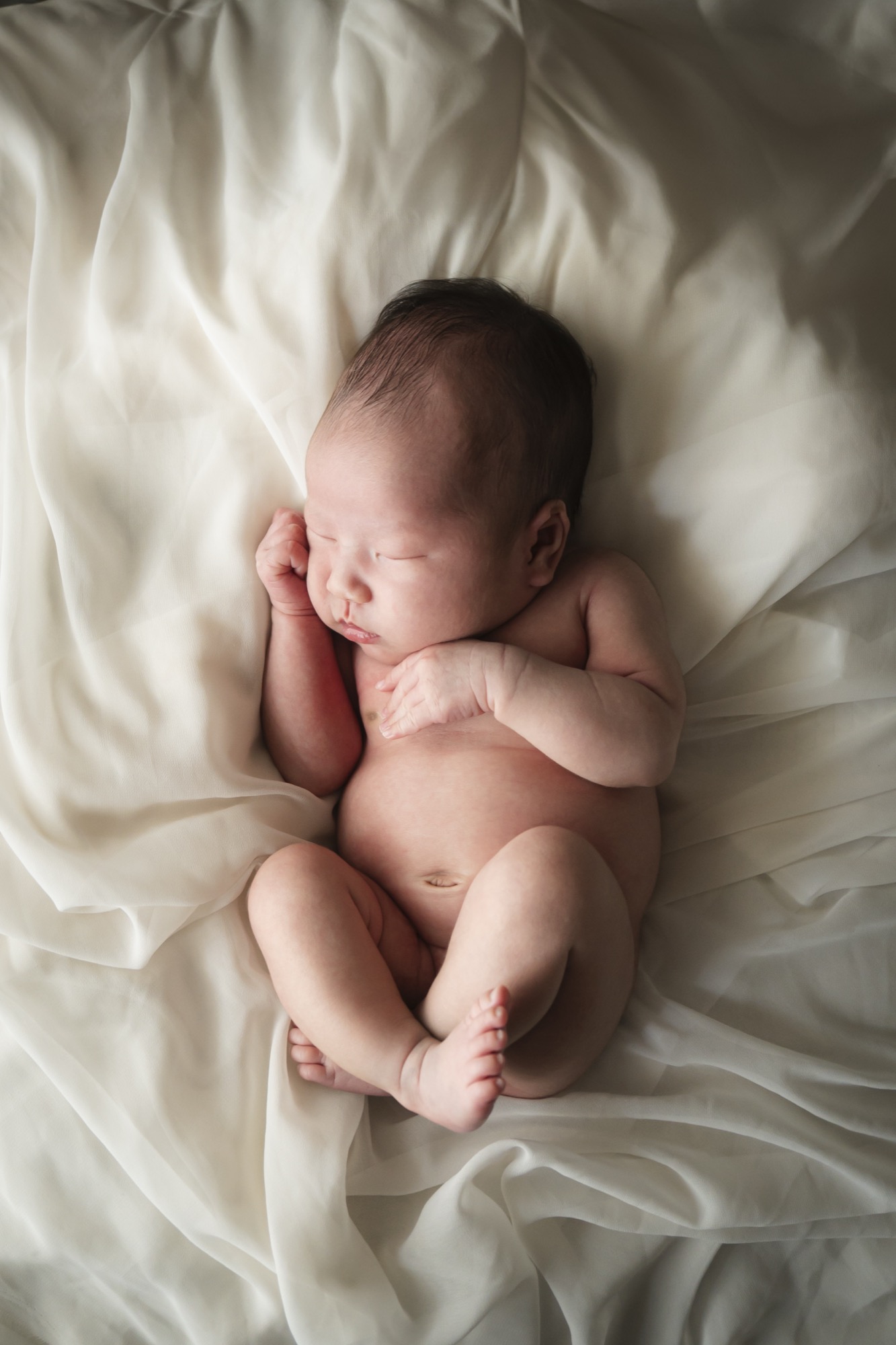 やわらかな光の中で眠る新生児を、真上から写した写真